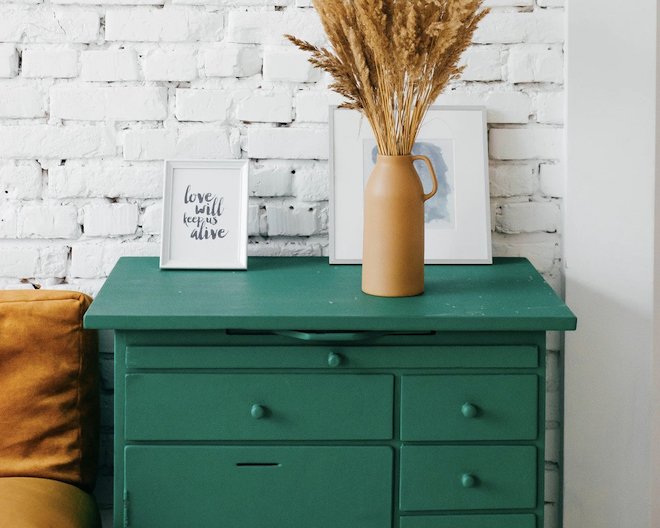 A green chest of drawers with yellow contrasting decoration elements.
